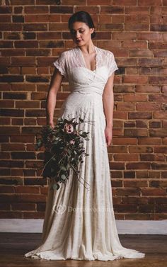 a woman standing in front of a brick wall wearing a white dress and holding a bouquet