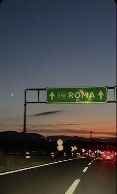 a street sign that reads roma above the highway at night with cars passing by in the foreground