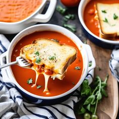 a spoon full of soup with bread and tomatoes in the bowl next to it on a cutting board