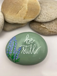 painted rocks with the words be still written on them next to some flowers and leaves