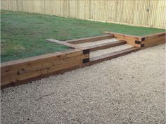 a wooden bench sitting in the middle of a graveled area next to a fence