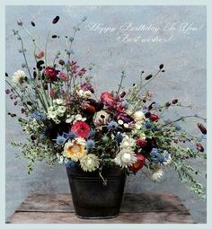 a vase filled with lots of colorful flowers on top of a wooden table next to a wall