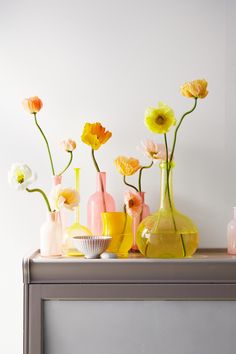 several vases with flowers in them sitting on a shelf next to each other,