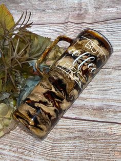 an empty glass bottle sitting on top of a wooden table next to leaves and flowers