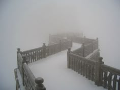 a snow covered bridge with railings and gates in the foggy weather on a snowy day