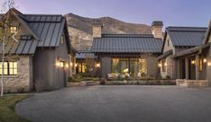 a large house with lots of windows and lights on it's front porch, surrounded by mountains