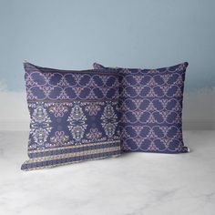 two purple and blue decorative pillows on a white table with a blue wall in the background