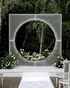 an outdoor ceremony setup with white flowers and greenery in front of a circular mirror