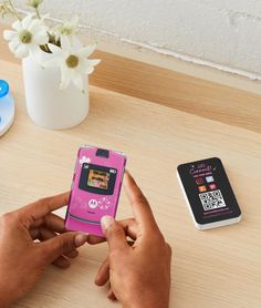 a person holding a pink cell phone next to a couple of other items on a table