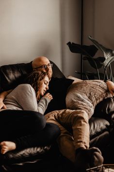 a man and woman laying on a couch with their arms around each other as they look at something in the distance