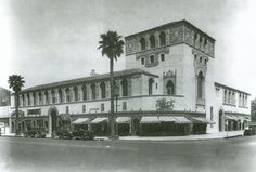 an old black and white photo of a building with palm trees on the street corner