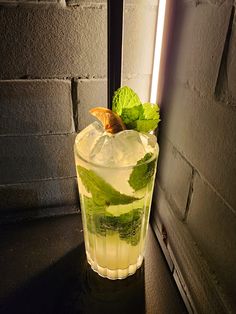 a tall glass filled with ice and mint on top of a table next to a brick wall