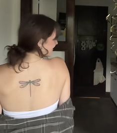 a woman with a dragonfly tattoo on her back is standing in front of a mirror