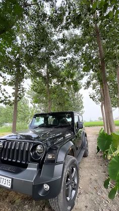 a black jeep parked on the side of a dirt road next to some green trees