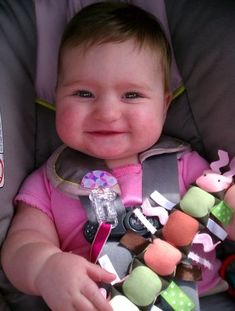 a baby sitting in a car seat with toys on it's back and smiling at the camera