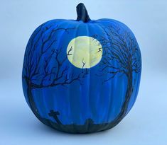 a blue painted pumpkin with trees and moon in the sky on it's side