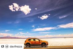 an orange car parked on the side of a road in front of a blue sky