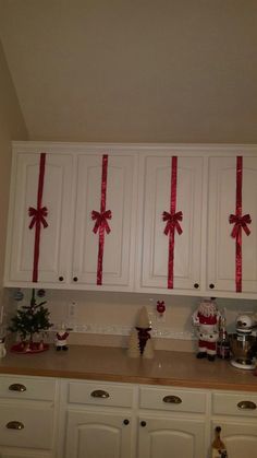 a kitchen with white cabinets and red bows on the back of the cupboards that have been decorated for christmas