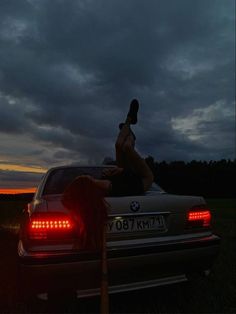 a woman sitting on the back of a car at night with her legs up in the air