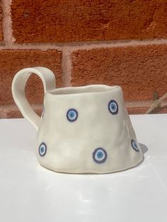 a white ceramic pitcher with blue eyes on it's side sitting next to a brick wall