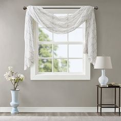 a white curtain hanging over a window next to a table with a vase on it