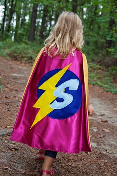 "We are proud of this quality custom superhero cape, which ships in 2-3 business days. This listing is for the exact color combinations shown above, with your choice of initial (or number if you prefer). If purchased you will receive: Pink satin cape (yellow lining), blue felt circle, yellow felt lightning bolt, light blue felt letter If you would like the felt embellishments (shapes/initial) to be in different colors please send me a convo. Our satin capes are HANDMADE MADE IN THE USA and measu Lightning Bolt Light, Buzz Lightyear Wings, Cape Superhero, Wooden Doll Cradle, Super Hero Cape, Superhero Party Favors, Halloween Capes, Trees For Kids, Girls Cape