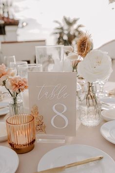 the table is set with white plates and silverware, gold vases and flowers