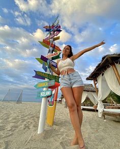 a woman standing next to a sign on top of a sandy beach