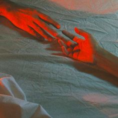 two hands reaching out to each other on a bed with white sheets and red light