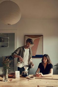 a man and woman sitting at a wooden table in front of a potted plant