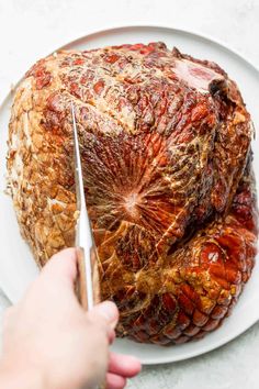 someone is cutting into a large piece of meat on a white plate with a knife