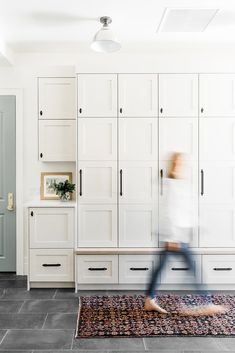 a blurry photo of a person running in a room with white cabinets and rug