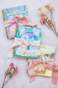 some books and flowers are laying on the table together with pink ribbon tied around them