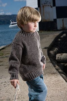 a young boy walking on the beach with a frisbee in his hand and a boat in the background