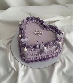 a purple heart shaped cake on a white tablecloth with pearls and two wedding rings in the middle