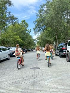 three children are riding bikes down the street in front of parked cars and suvs