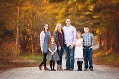 a family posing for a photo in the middle of an autumn forest with leaves on the ground