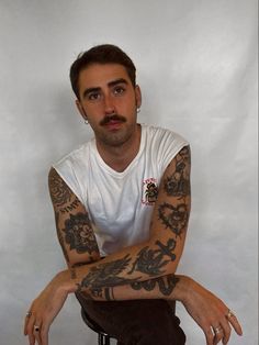 a man with tattoos on his arms and legs sitting in front of a white background