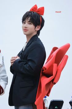 a man in a black jacket and red bow tie standing next to another person with his arms crossed