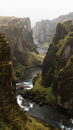 a river flowing through a lush green valley surrounded by tall rocks and moss covered mountains