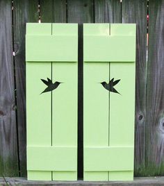 two green doors with birds painted on them in front of a wooden fence and string lights