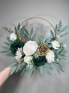 a hand holding a flower arrangement in front of a gray wall with green leaves and white flowers