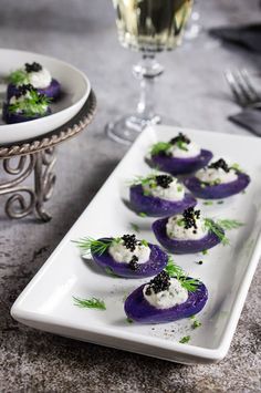 small appetizers are arranged on a white plate next to a glass of wine