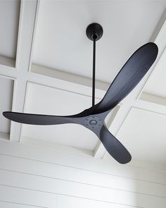 a ceiling fan hanging from the ceiling in a room with white walls and paneling