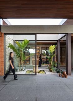 a woman walking in front of a building with glass doors and palm trees on the outside