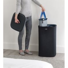 a woman standing next to a trash can holding a blue bag in her right hand