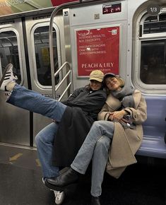 two people sitting on a subway car with their feet up and one person laying down