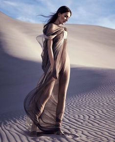 a woman standing in the sand wearing a dress