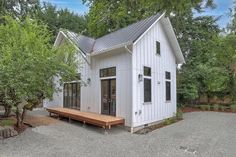 a small white house sitting in the middle of a yard with trees and gravel around it