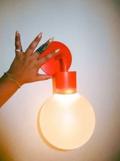 a woman's hand reaching for an object on top of a light fixture that is red and white